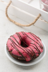 Chocolate donut/doughnut with raspberry glaze. White plate, white crate with rope handles