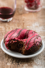 Chocolate donut/doughnut with raspberry glaze. Inside is shown through the bite, Wine and raspberries in the background 