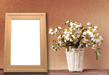 blank wooden frame mockup with basket of chamomile flowers on wooden table and brown paper wall in vintage tone.