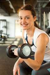 Fototapeta na wymiar Smiling woman holding dumbbells in gym.