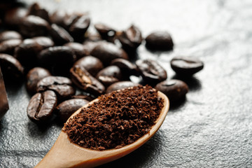 Coffee grounds in wooden spoon close to coffee beans on black gr