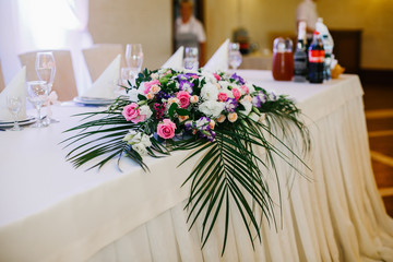 Large green leaves hang from colorful roses on dinner table