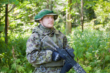 Military man in camouflage uniforms and flak jacket with a gun in the woods