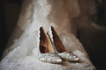 Elegant shoes decorated with crystals stand on bride's dress