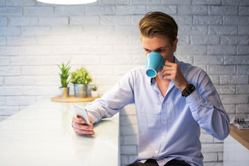 Young man drinking coffee and using smart phone at home.