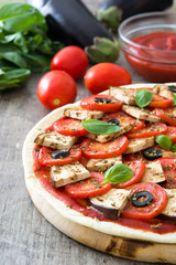 Vegetarian pizza with eggplant, tomato, black olives, oregano and basil on wooden background