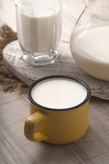 Glass, pitcher, yellow cup of kefir and napkin on a white table