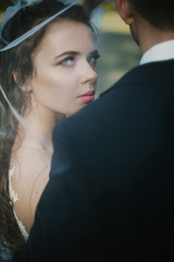 Stunning bride hidden under the veil looks over groom's shoulder
