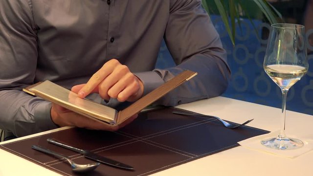 A man sits at a table in a restaurant and reads a menu