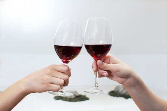 Two female hands toasting with red wine on bright background. Close up.