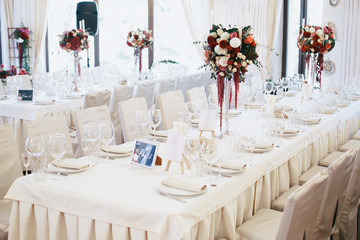Long white dinner tables decorated with tall bouquets of red spe