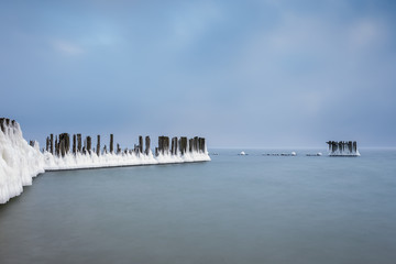 Winter landscape at the sea. Frozen wooden breakwaters line at Baltic Sea. Morning at Babie Doly, Poland. Long exposure photo.