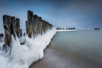 Winter landscape at the sea. Frozen wooden breakwaters line at Baltic Sea. Morning at Babie Doly,...