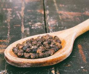 black pepper in wooden spoon on old rustic table closeup