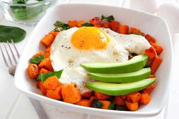 Breakfast nutrient bowl with sweet potato, egg, avocado and spinach, close up table scene