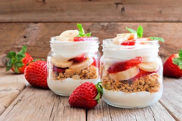 Healthy strawberry and banana parfaits in mason jars with a rustic wood background