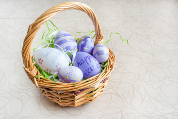 Easter wicker basket with colored eggs on white board.