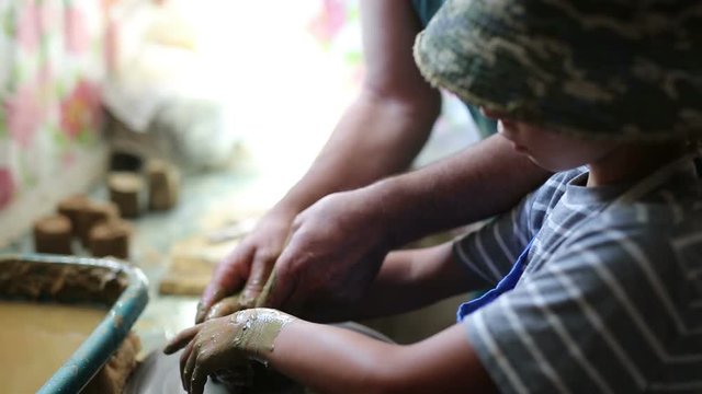 Senior potter teaching happy little boy the art of pottery. Child working with clay, creating modeling ceramic pot on sculpting wheel. Mentoring, generations concept. Pottery lessons workshop for kids