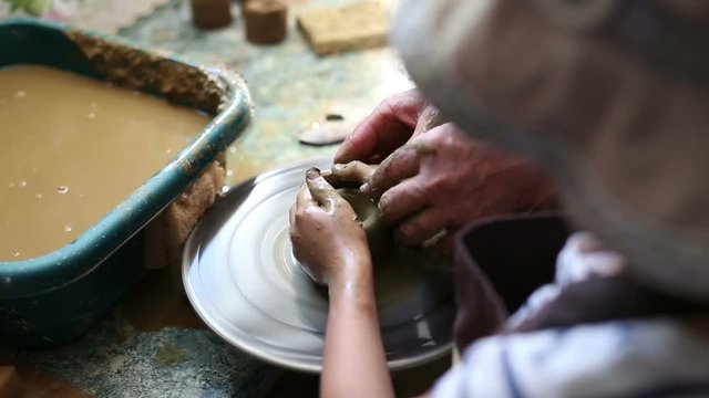 Senior potter teaching happy little girl the art of pottery. Child working with clay, creating modeling ceramic pot on sculpting wheel. Mentoring generations concept. Pottery lessons workshop for kids