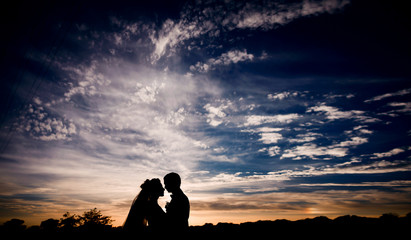 Silhouettes of wedding couple standing under dark blue sky with