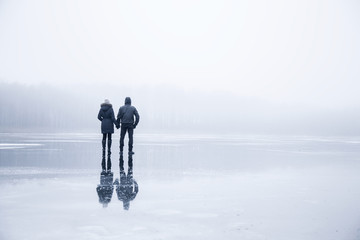 Couple in the mist walking on the lake ice in winter afternoon. Peaceful atmosphere. Foggy air.