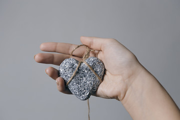 Hands holding a stone heart in jute bondage against grey background
