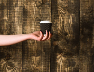paper or plastic coffee cup in hand on wooden background