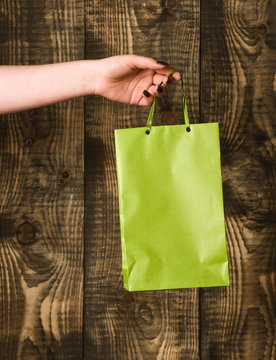 green shopping bag in female hand on wooden background