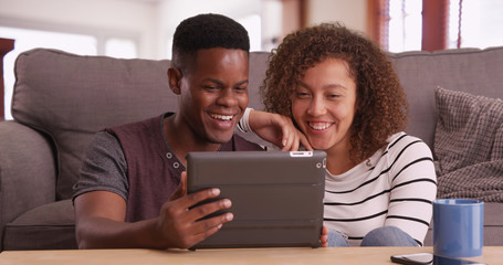 Authentic millennial black couple sits on floor watching a video on their tablet