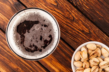 glass of dark cold frothy beer, nuts old wooden table