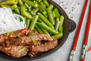 Fried spicy beef with sesame seeds, green beans and rice noodles. Dinner in the Asian style. Selective focus
