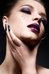 Young woman with creative make-up and violet lips with a gradient and sparkles on the face. Beautiful model with bright nails with rhinestones. The beauty of the face. The photo was taken in a studio.