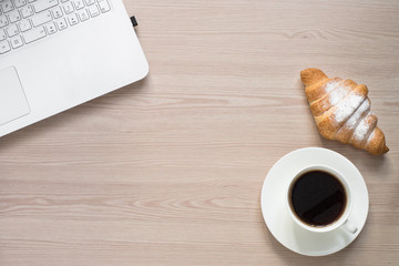Laptop, coffee and croissant at desk table. Coffee break at work in office