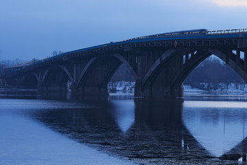 Frosty early morning. Metro bridge reflected in the water. The first metro train moves on the bridge. Kyiv. Ukraine