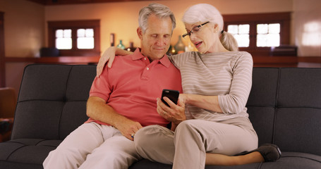 Senior couple sitting on couch using smartphone