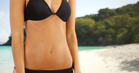 Young white girl stands on a Caribbean beach in her black bikini