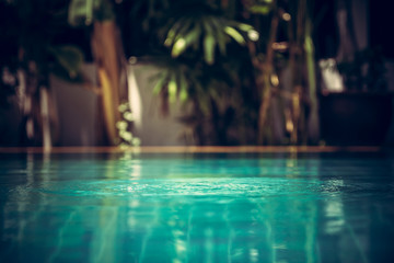 Swimming pool background in vintage style with ripples on turquoise water and tropical plants on...