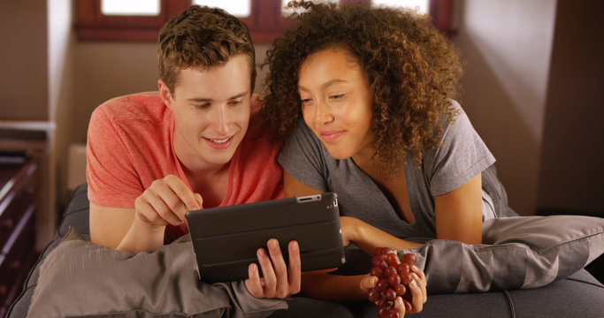 Cheerful couple using digital tablet on couch.