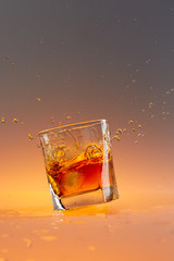 standing whiskey glass with drops and ice cube