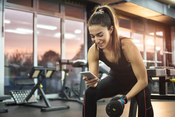Young woman using phone in gym.