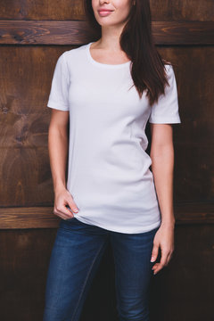 Young woman wearing blank white t-shirt with area for your logo or design, mock-up of template white t-shirt, wooden wall in the background