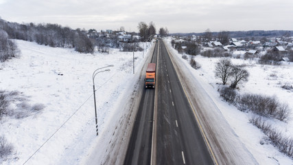 Semitrailer trucks driving on winter three lane asphalt highway in village. Aerial view