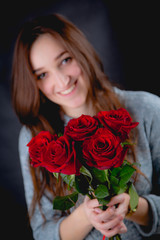 Pretty girl is holding a bouquet of red roses, dark background