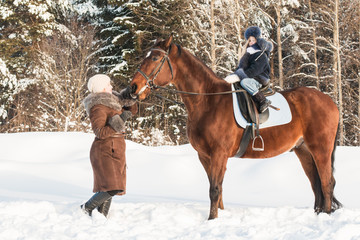 Fototapeta premium Small girl and mom near horse in a winter