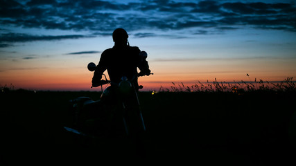 The silhouette of a man on a motorbike at sunset