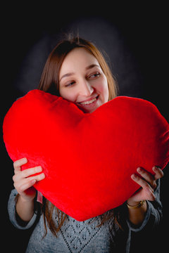 Pretty girl is holding big red heart on dark background