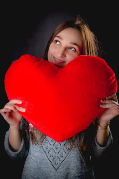 Pretty girl is holding big red heart on dark background