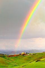 Rainbow after rain over green field with flock of sheep and traditional rural home in Tuscany region, Italy. Wonderland concept. Vertical format.