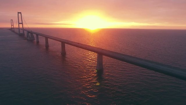 An aerial view of the traffic on Storebaelt bridge over sea in Denmark with sunset in background.