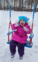 Happy child girl on swing in sunset winter. Little kid playing on a winter walk in nature